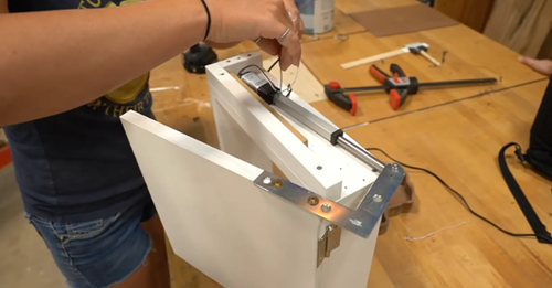 Installing a mini linear actuator inside a custom cabinet for automated door opening.